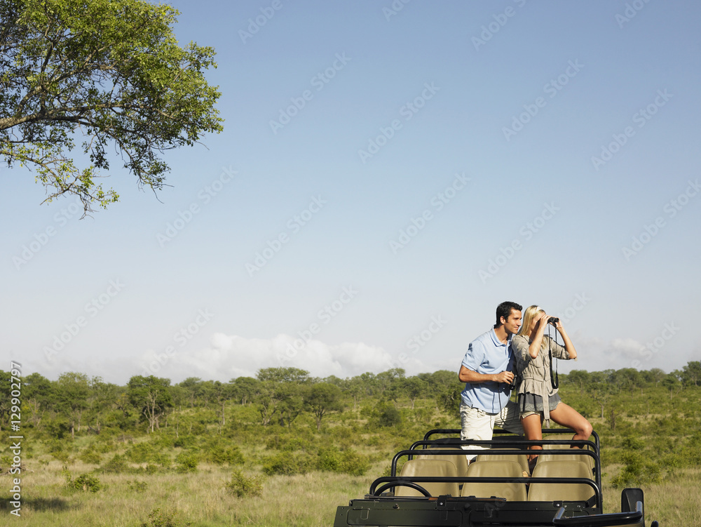 Young couple on safari standing in jeep and looking through binoculars Young couple on safari standing in jeep and looking through binoculars
