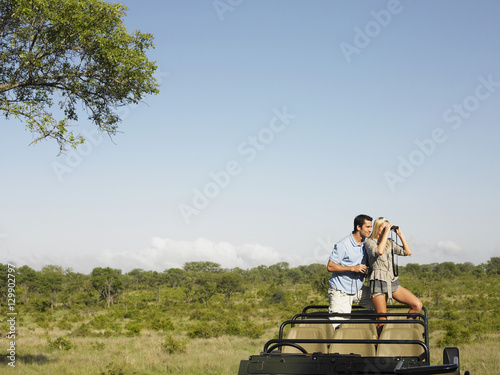 Young couple on safari standing in jeep and looking through binoculars © moodboard