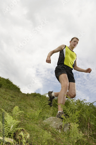 Low angle view of a male hiker jogging on grassy landscape against sky