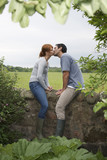 Full length side view of a couple kissing on countryside wall against landscape