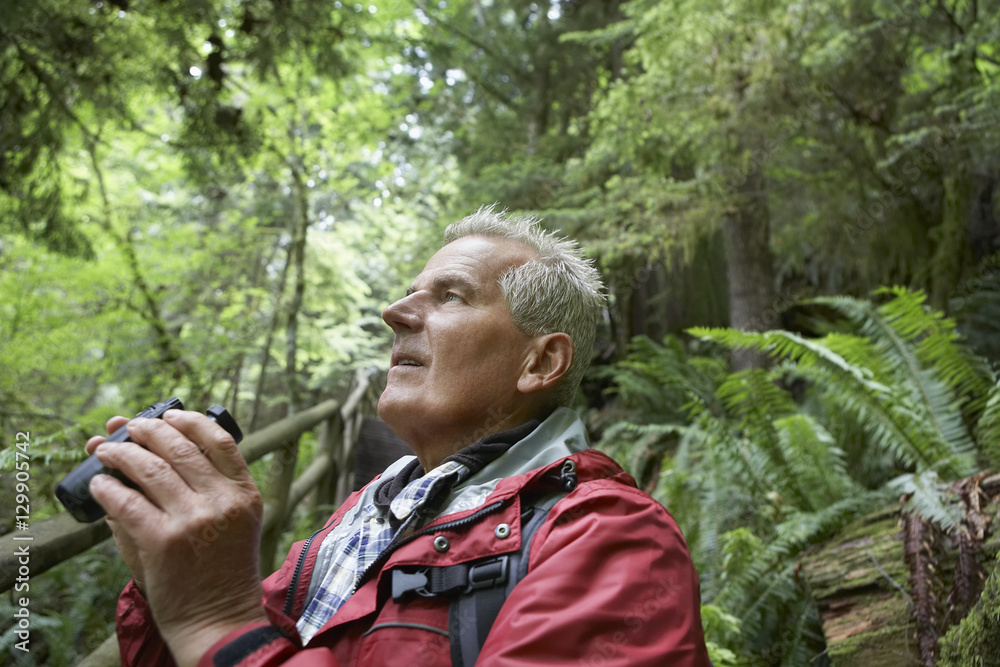 Side view of a mature man looking up with binoculars in the forest Side view of a mature man looking up with binoculars in the forest