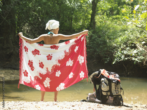 Φωτογραφία Rear view of a young woman wrapping herself with sarong by backpack and forest l