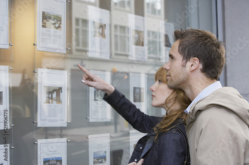 Side view of a young couple looking at window display at real estate office photo