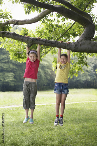 Full length of little girls hanging from tree branch