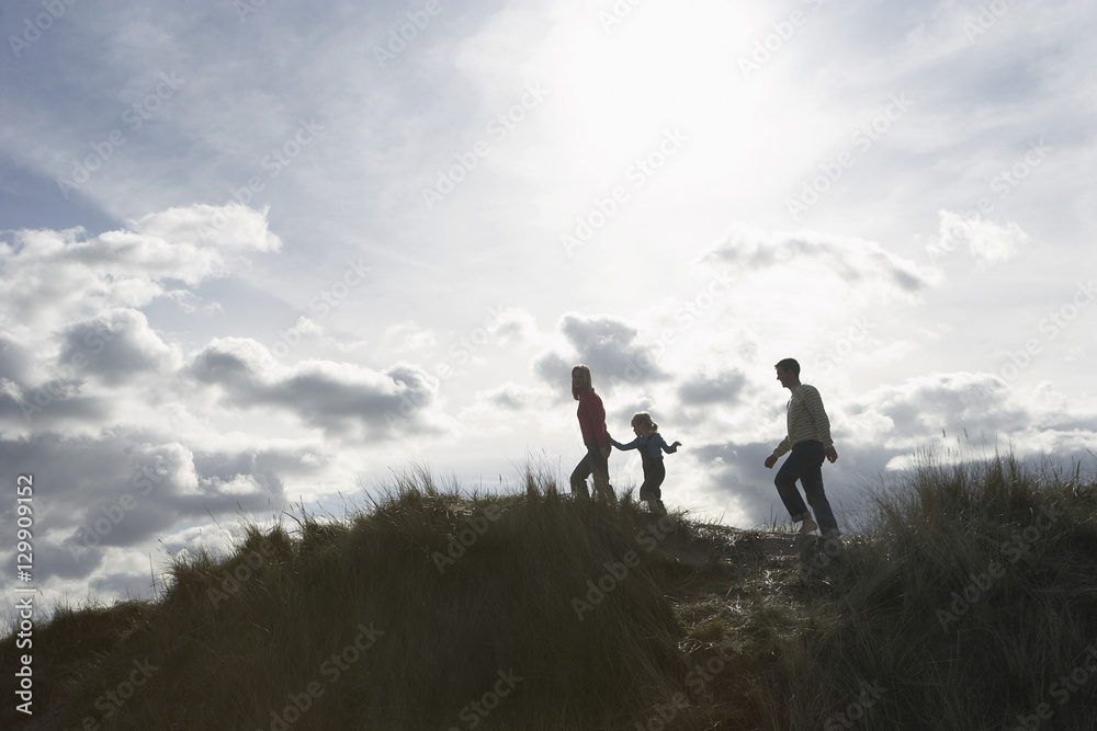 Silhouetted image of parents and daughter walking on sand dunes at beach