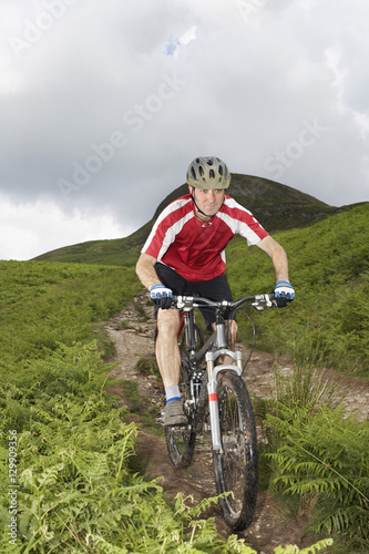 Male cyclist on countryside track against hill and sky