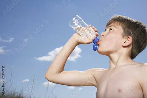 Φωτογραφία Side view of a shirtless boy drinking from water bottle against sky