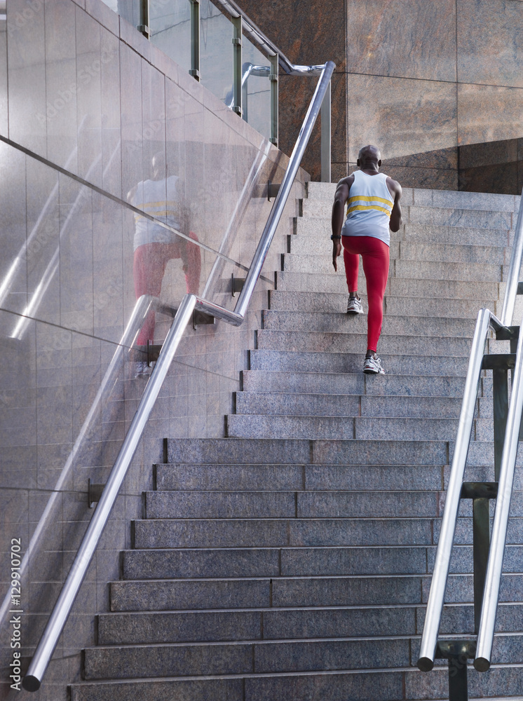 Rear view of a male athlete running up staircase outside building