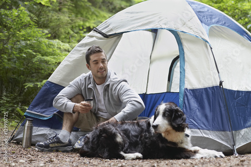 Smiling young man sitting by tent with his pet dog