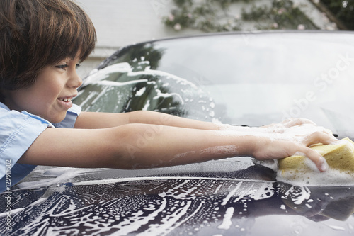 Closeup side view of a young boy washing car with sponge
