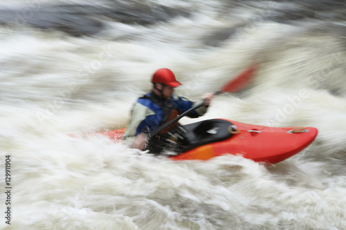 Side view of a blurred man kayaking in rough river