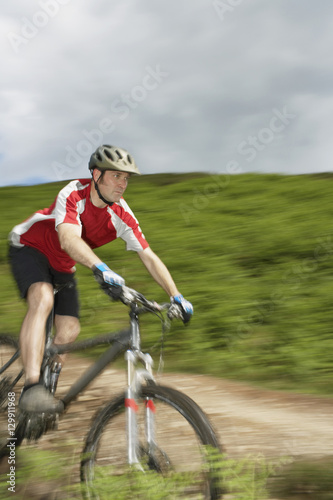 Male cyclist on countryside track against hill and sky