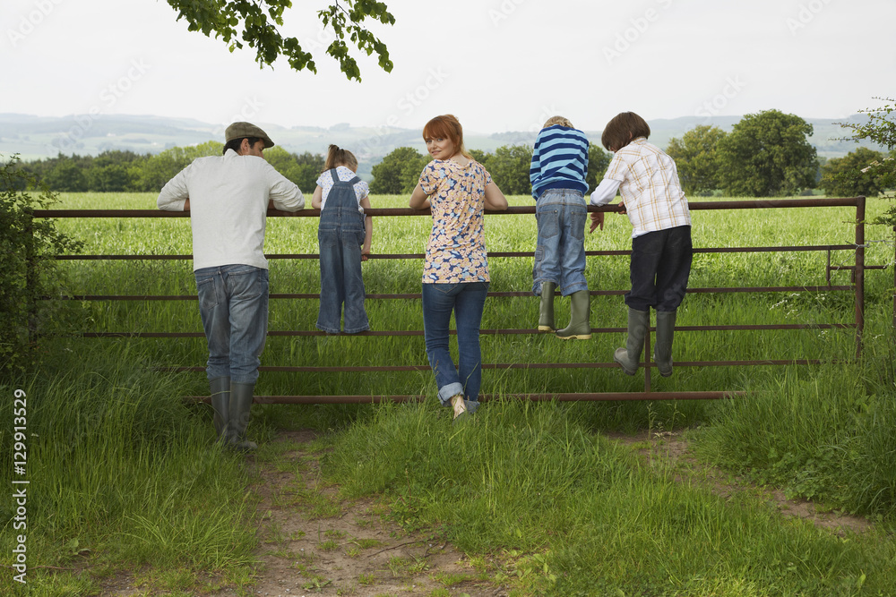 Obraz premium Full length rear view of couple with three children looking at lush landscape by fence