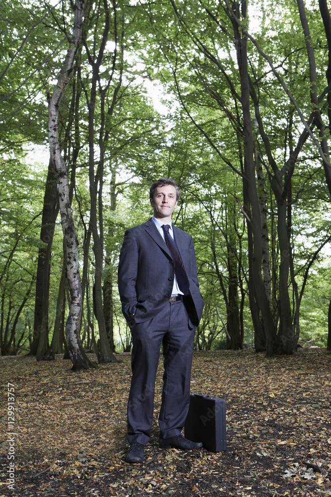 Fototapeta premium Full length portrait of confident businessman with hands in pockets standing in forest