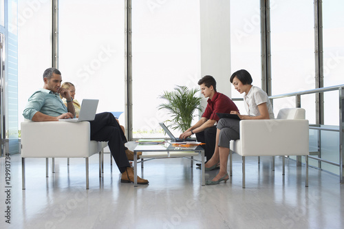 Full length side view of four business people sitting in modern waiting room at office