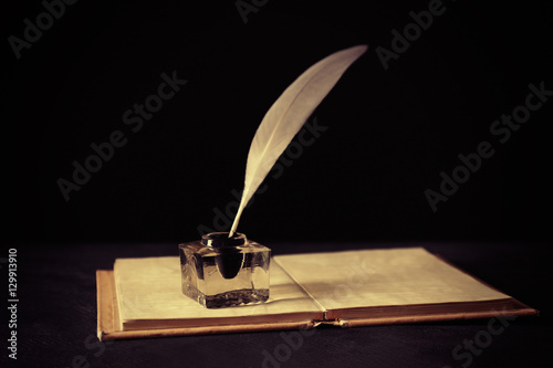 Feather pen with inkwell and open notebook on dark background