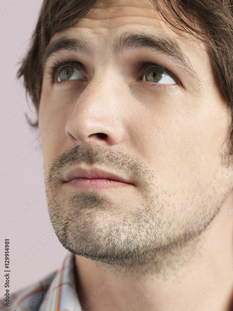 Closeup of confused young man looking up isolated on colored background