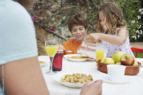 Two young children having breakfast at the outdoor table