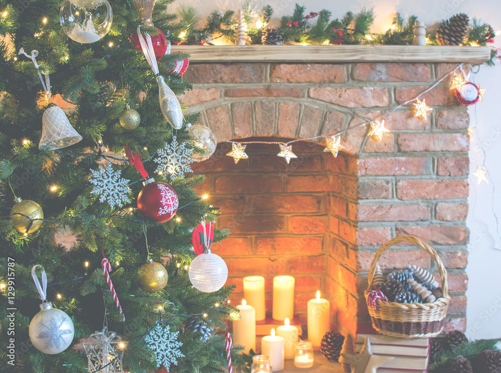 Obraz premium Christmas setting background: decorated Christmas tree, pine cones in the basket with fireplace on the background; candles an baubles, selective focus; toned photo