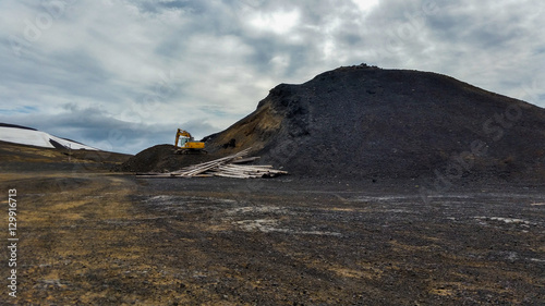 Excavator digging near mountain of dirt in barren landscape Iceland