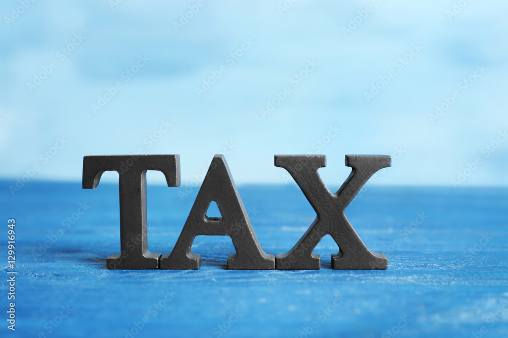 Fototapeta premium Word TAX on blue wooden surface, close up view