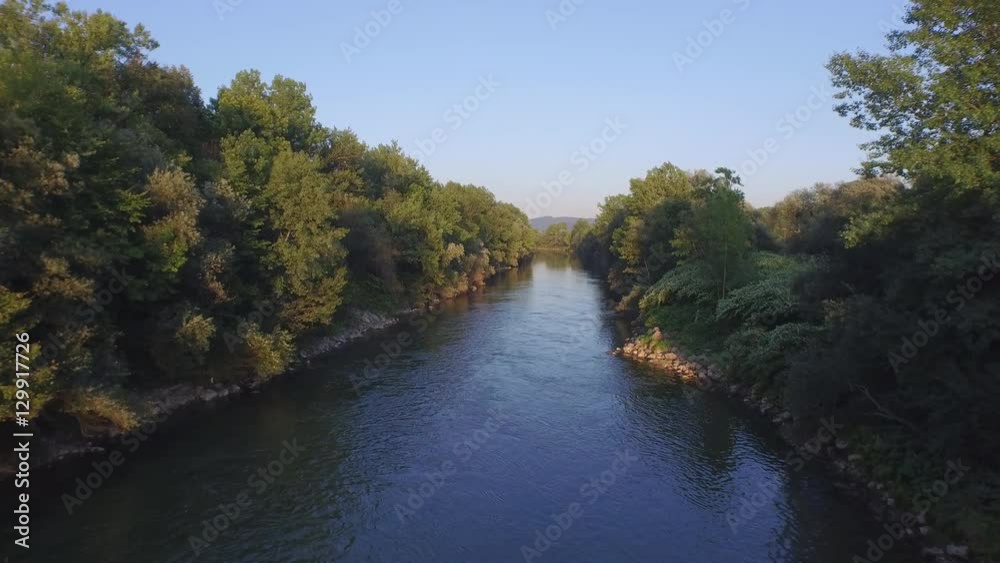 AERIAL: Wide green river with rocky and overgrown lush riverbank AERIAL: Wide green river with rocky and overgrown lush riverbank