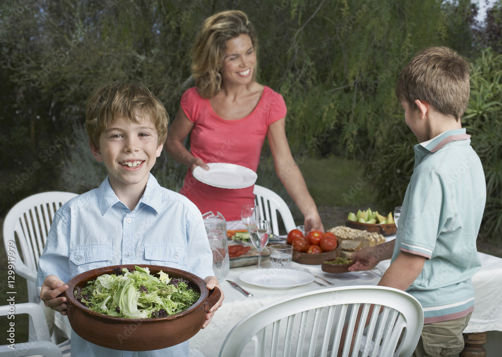 Mother and two sons setting the dinner table in garden Mother and two sons setting the dinner table in garden