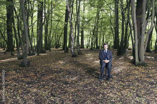 Full length portrait of businessman sitting in middle of forest