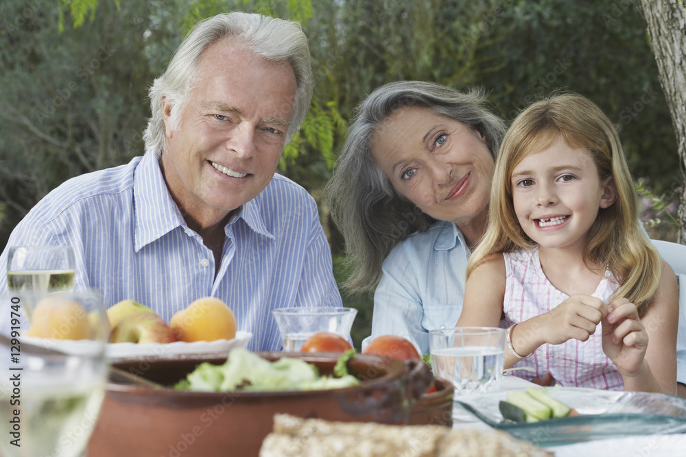 Portrait of grandparents with granddaughter sitting at garden table