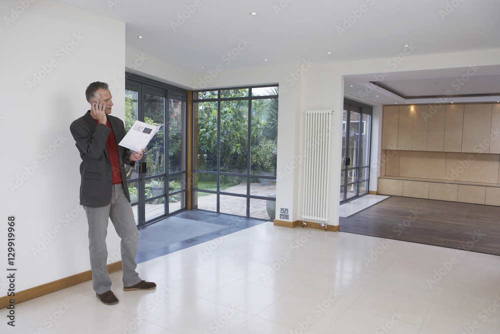 Full length of a male real estate agent using mobile phone in new