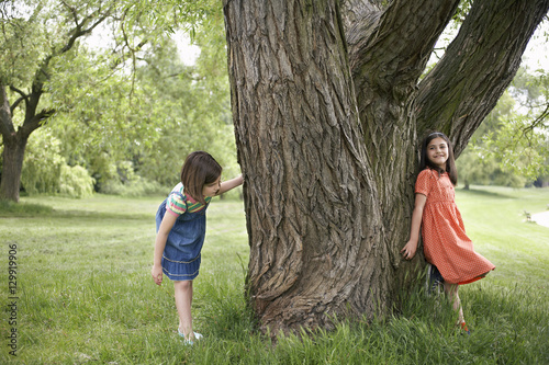 Full length of two girls playing hide and seek by tree