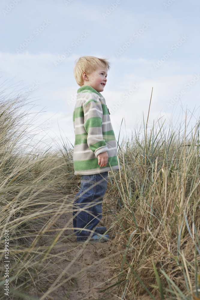 Side view of happy young boy standing on path among long grass Side view of happy young boy standing on path among long grass
