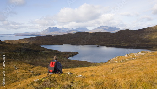 Hiker looking across Loch Dhughaill towards the distant Cuillin Hills, Sleat Peninsula, near Tarskavaig, Isle of Skye, Highland, Scotland photo