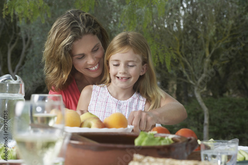 Smiling mother and daughter sitting at garden dining table