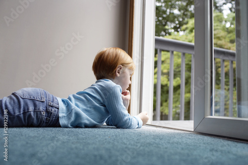 Side view of little girl looking out through balcony while lying on carpet at home