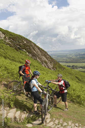 Happy three cyclists with bikes against lush landscape and clouds
