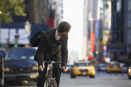 Photography Young businessman looking over shoulder while riding bicycle on urban street