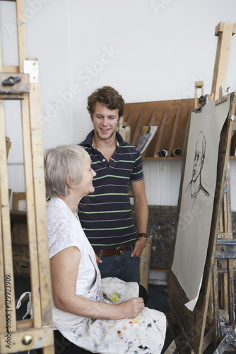 Young man looking at mature artist draw portrait in studio