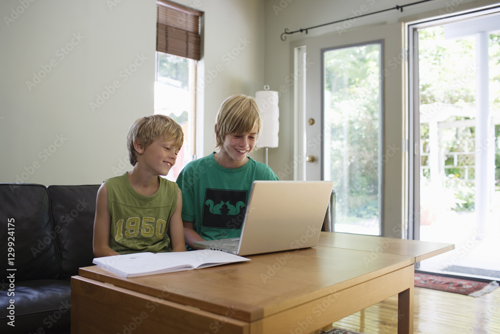 Happy young brothers using laptop at table in house Happy young brothers using laptop at table in house