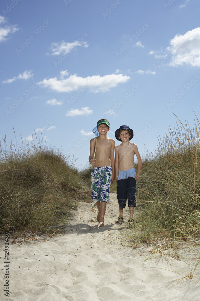 Full length portrait of two boys walking on sand dunes with fishing net