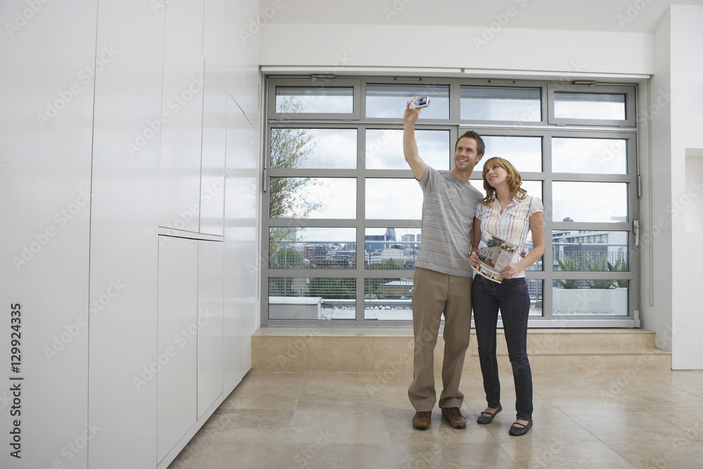 Full length of a smiling young couple photographing empty apartment Full length of a smiling young couple photographing empty apartment