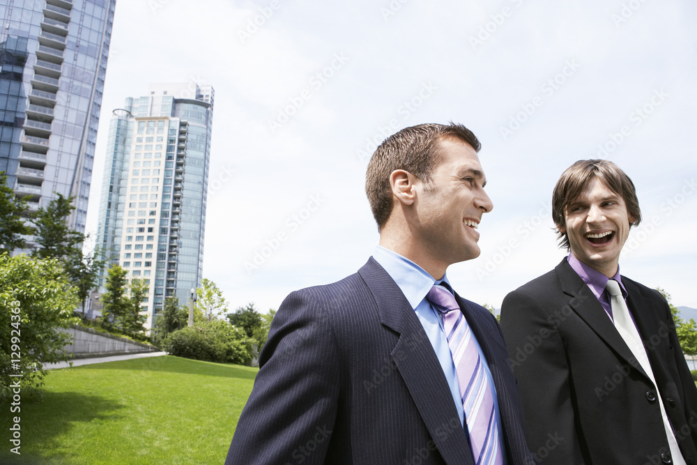 Two cheerful young businessmen laughing near office buildings Two cheerful young businessmen laughing near office buildings