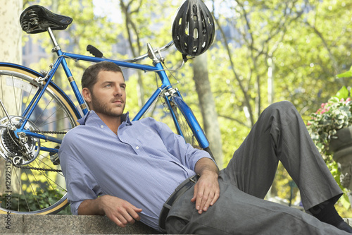 Handsome young businessman relaxing by bicycle in park