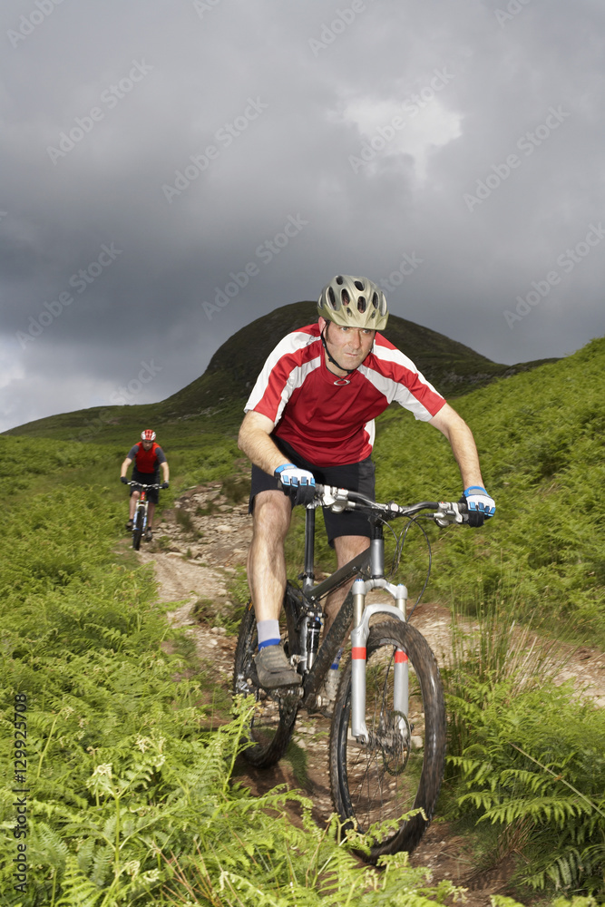 Two cyclists on countryside track against hill and sky Two cyclists on countryside track against hill and sky