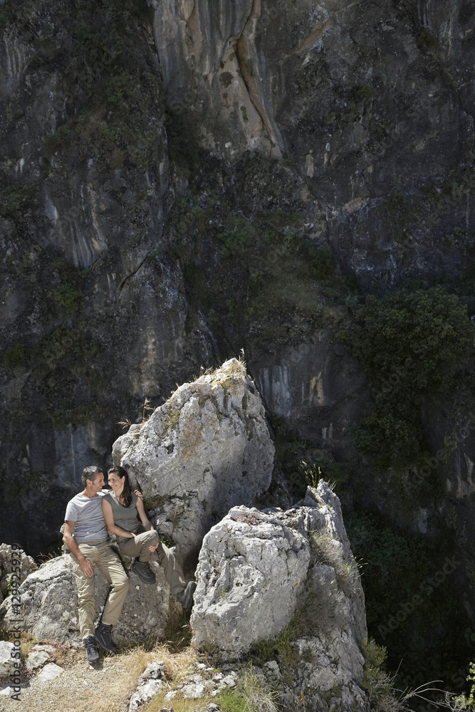 Elevated view of a relaxed couple sitting on rocks against mountains Elevated view of a relaxed couple sitting on rocks against mountains