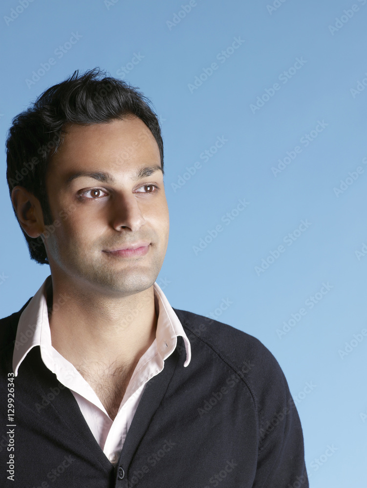 Closeup of handsome young man looking away and smiling on blue background Closeup of handsome young man looking away and smiling on blue background