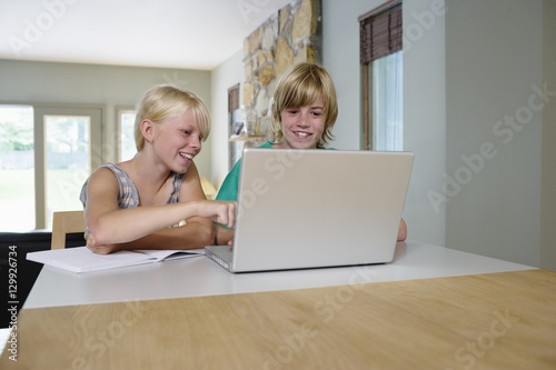 Smiling sister and brother using laptop at table in house