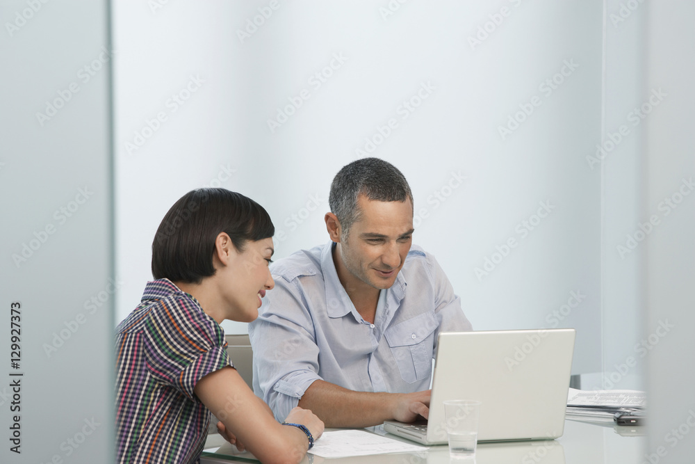Smiling man and female colleague using laptop in office Smiling man and female colleague using laptop in office