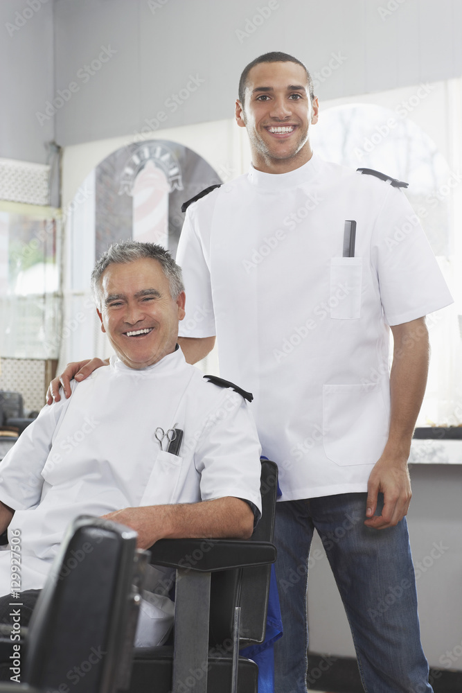 Portrait of two barbers in uniforms smiling at hair salon