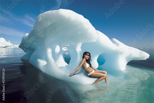 Beautiful young woman in bikini sitting on iceberg